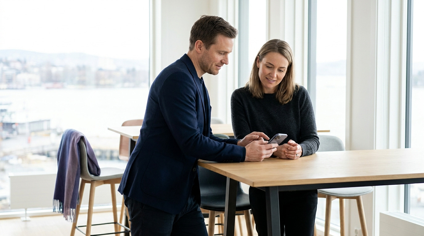 To norske bedriftsledere vurderer mobilavtale sammen på et moderne kontor
